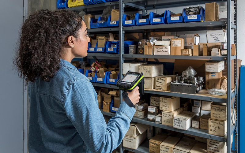 Woman uses mobile RFID scanner to locate a box of parts on a warehouse rack.