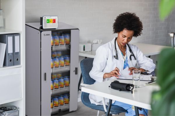 Healthcare worker sitting in front of device storage cabinet in hospital setting.